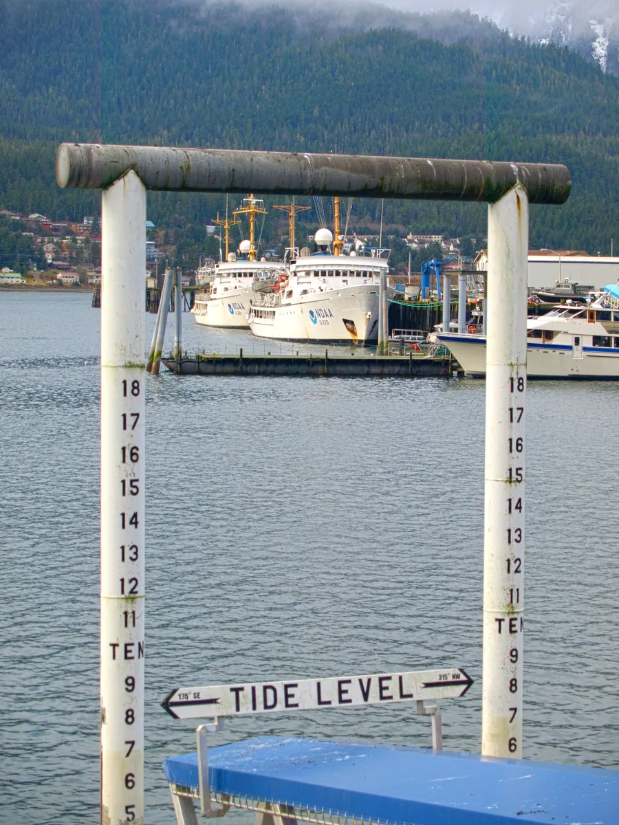 Staff gauge tide level di sebuah dermaga di Juneau, Alaska Tenggara, dengan kapal-kapal NOAA bersandar di latar belakang
